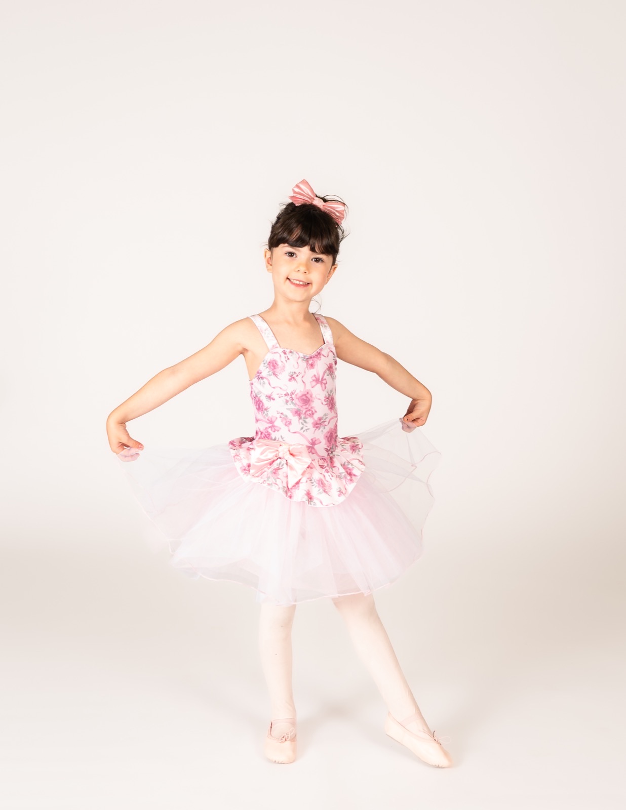 Three and four year old dancer holding out a pink floral tutu